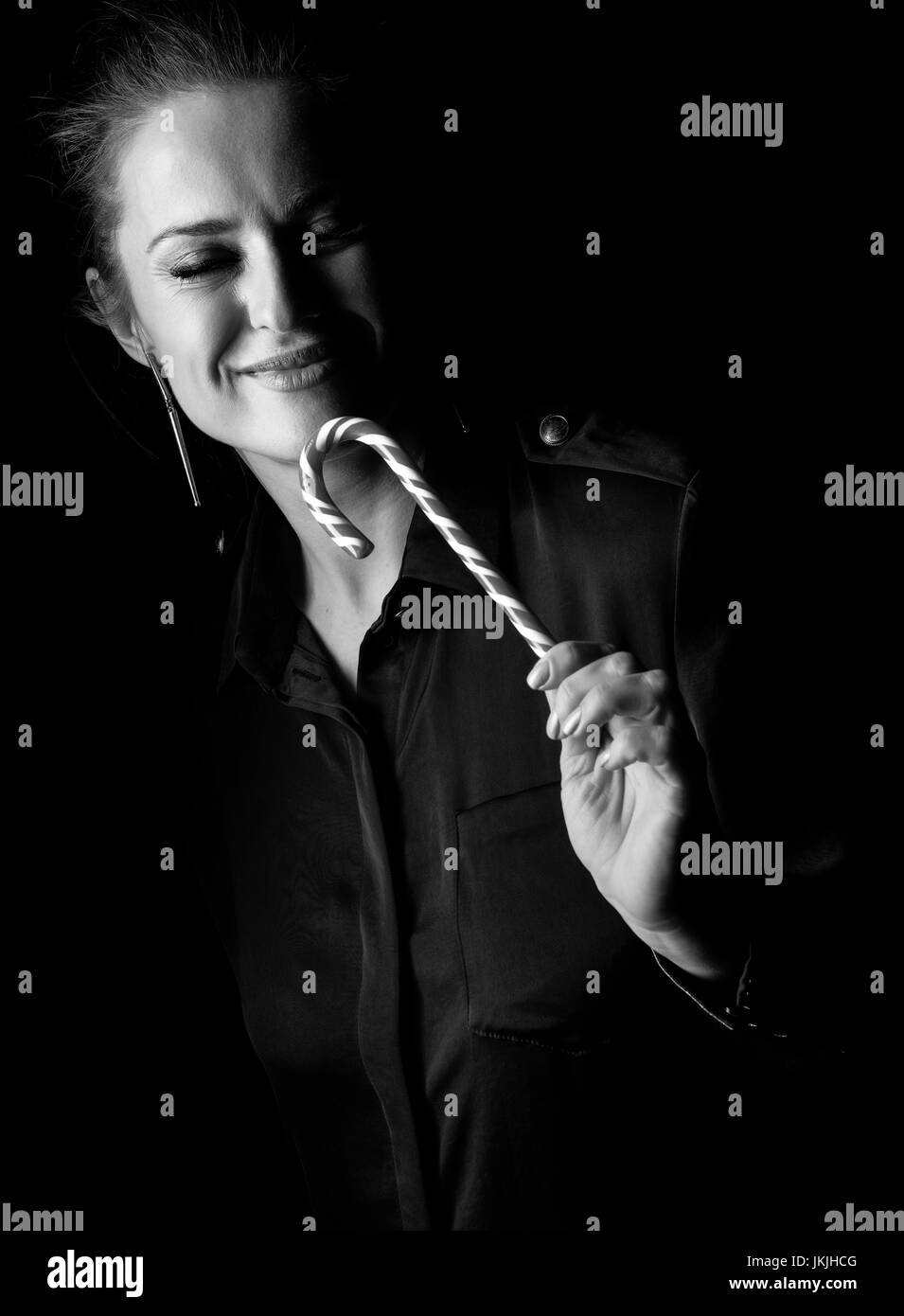 Сoming out into the light. smiling woman in the dark dress isolated on black enjoying christmas candy cane Stock Photo