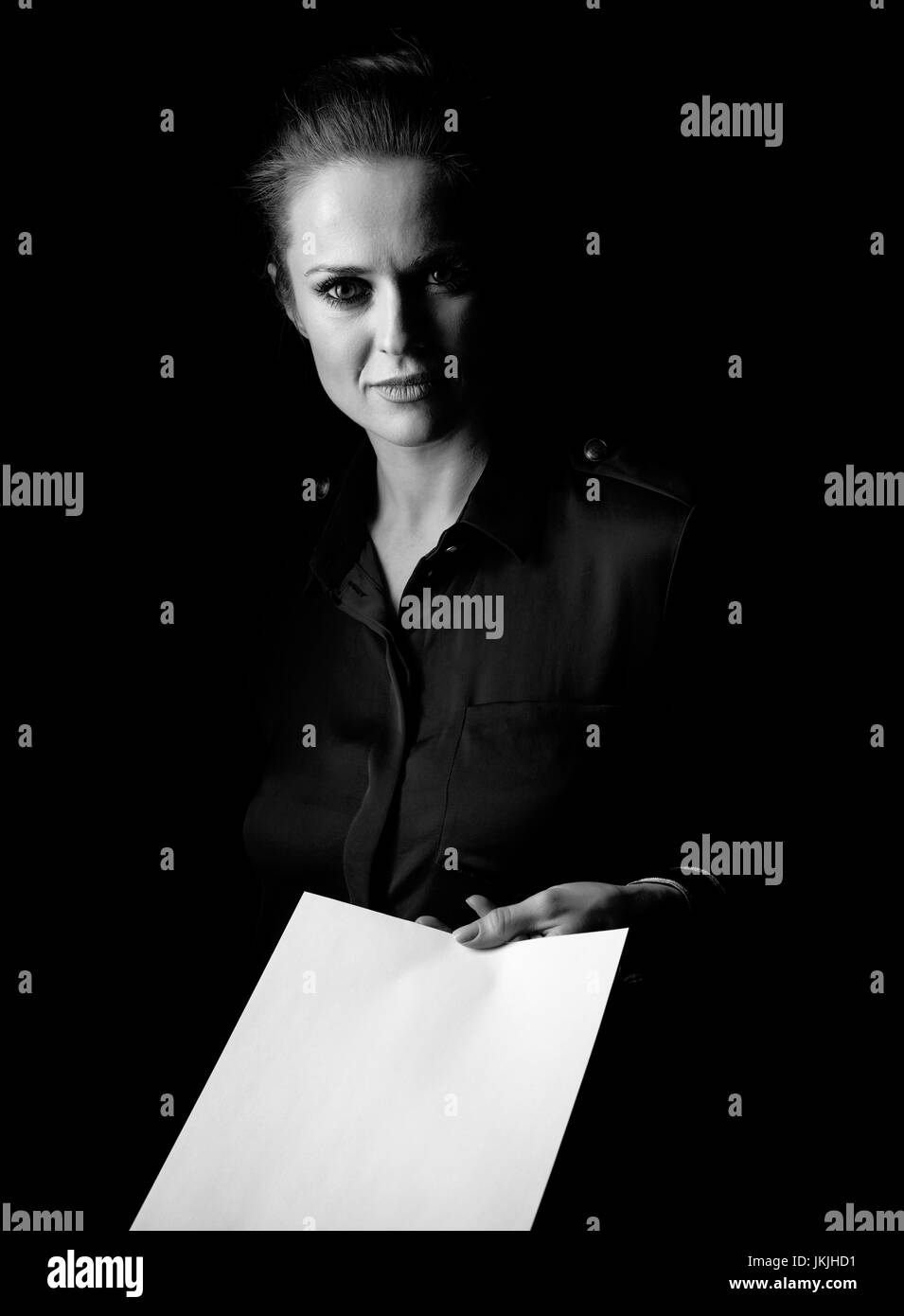 Сoming out into the light. Portrait of woman in the dark dress isolated on black giving paper sheet Stock Photo