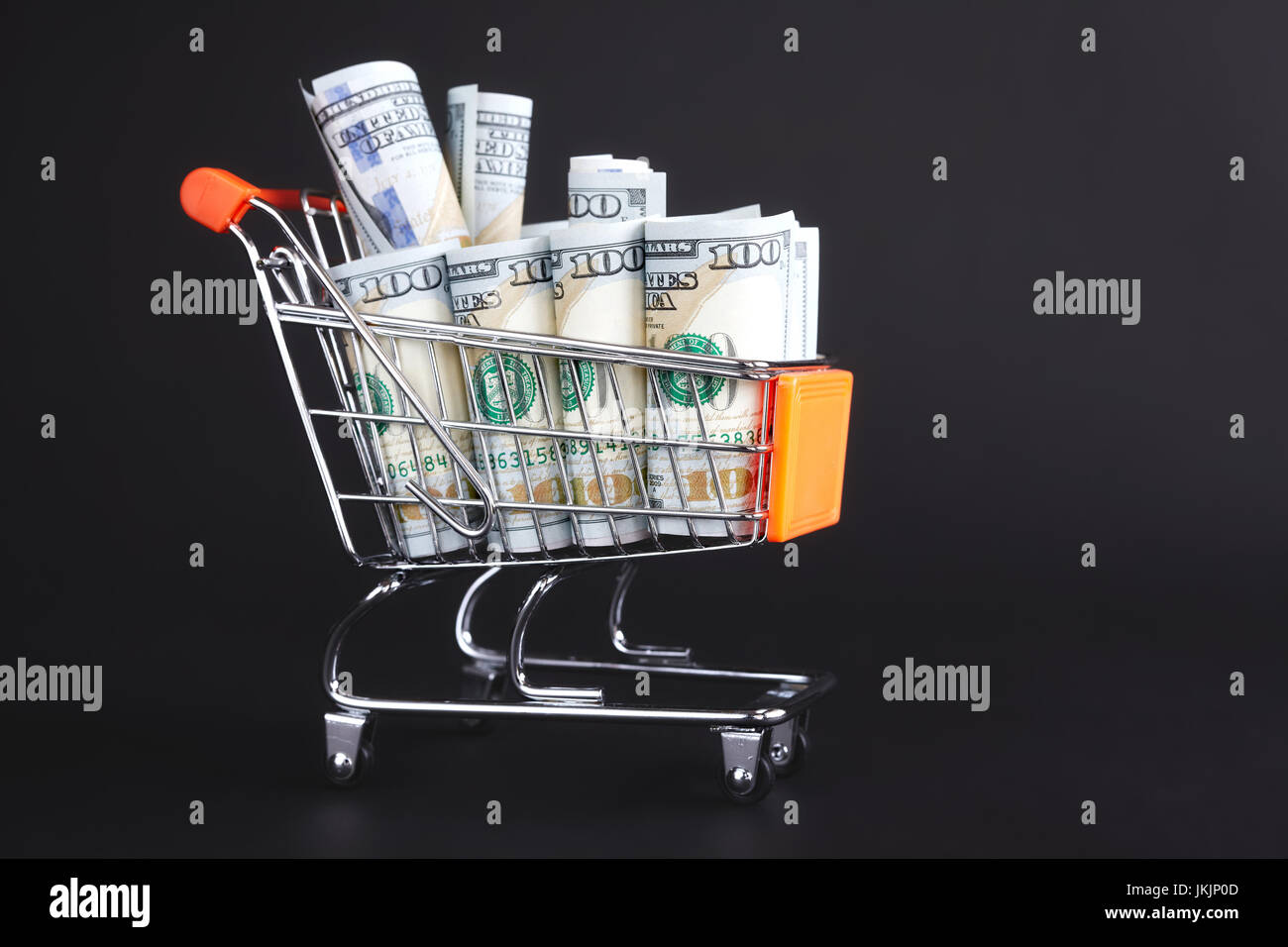 Shopping cart filled with one hundred dollar bills on a dark background. Stock Photo