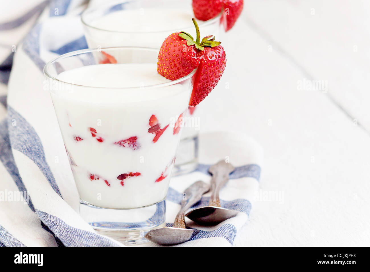 Dessert yogurt and strawberry layers in a glass on a blue striped napkin on a white background
