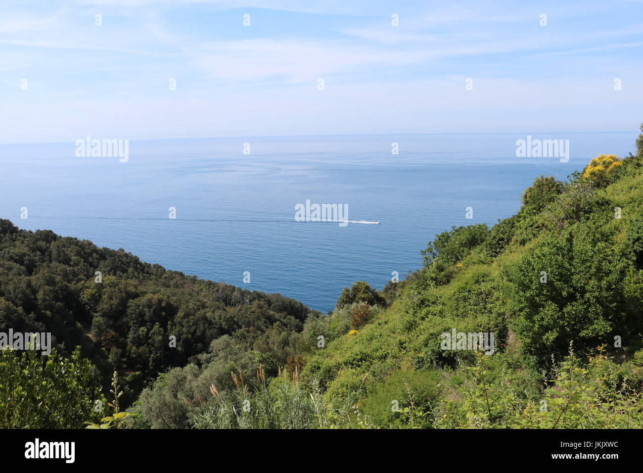 Clear blue sea and sky with a boat speeding across the landscape view seen from a trekking trail between the villages in Cinque Terre, Italy Stock Photo
