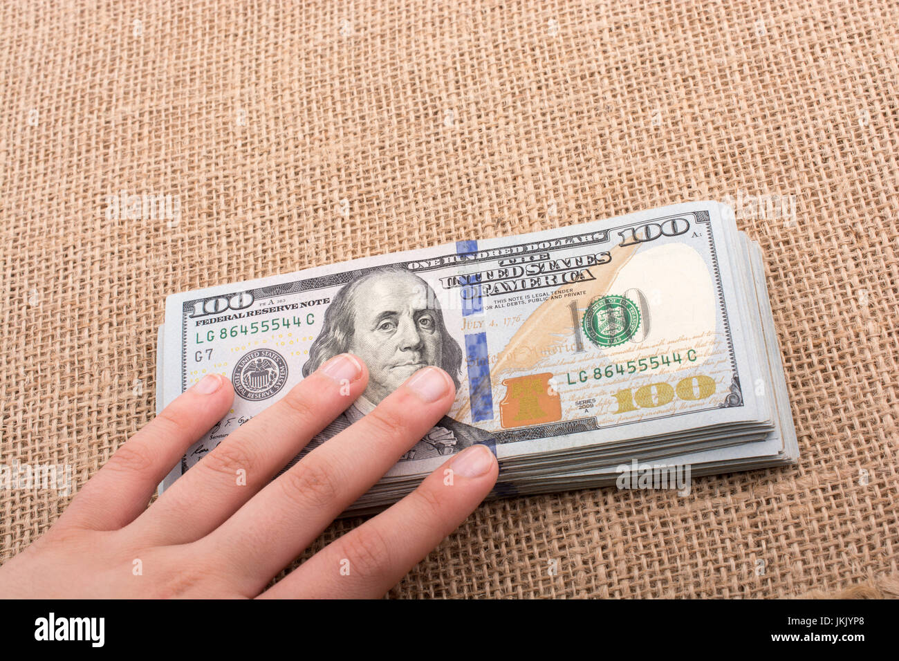 Hand holding banknote bundle of US dollar on a linen canvas background ...