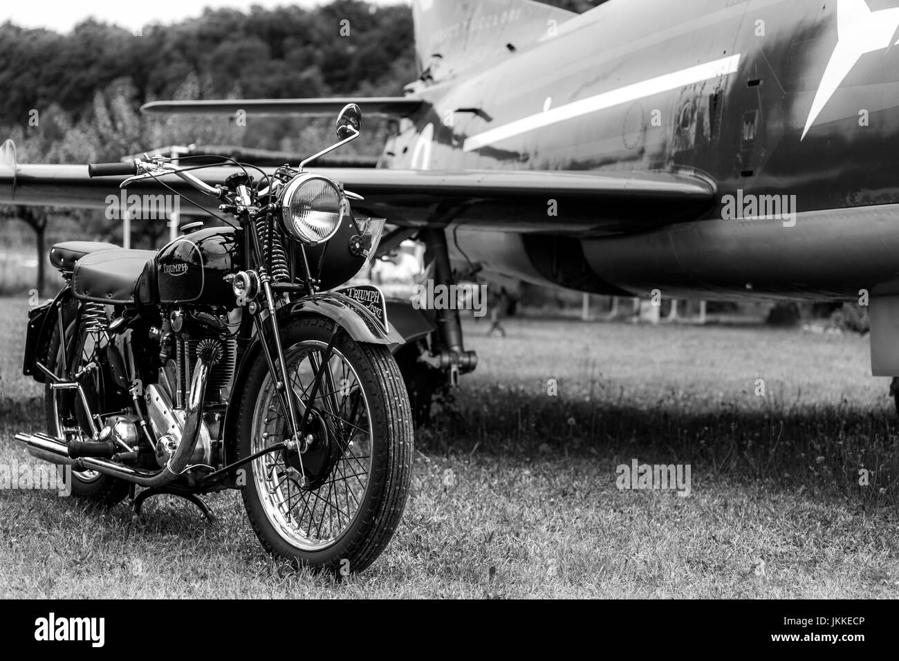 Old, black motorcycle made by Triumph Motorcycles - british brand with an airplane in the background. Black and white. Stock Photo