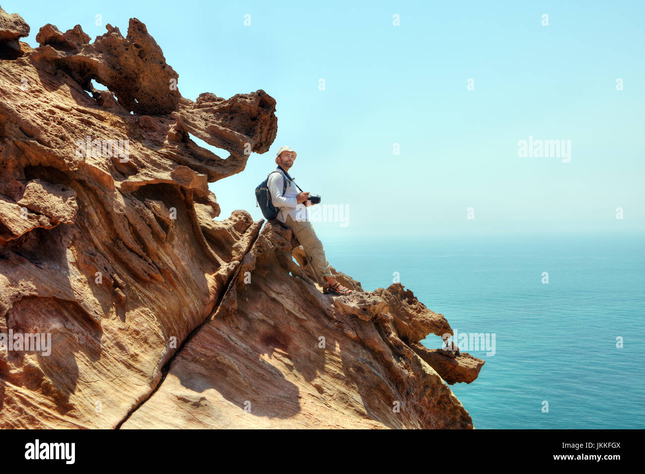 Nature photographer with a camera standing on the edge of the cliff above the sea, Hormuz Island, Hormozgan Province, southern Iran. Stock Photo