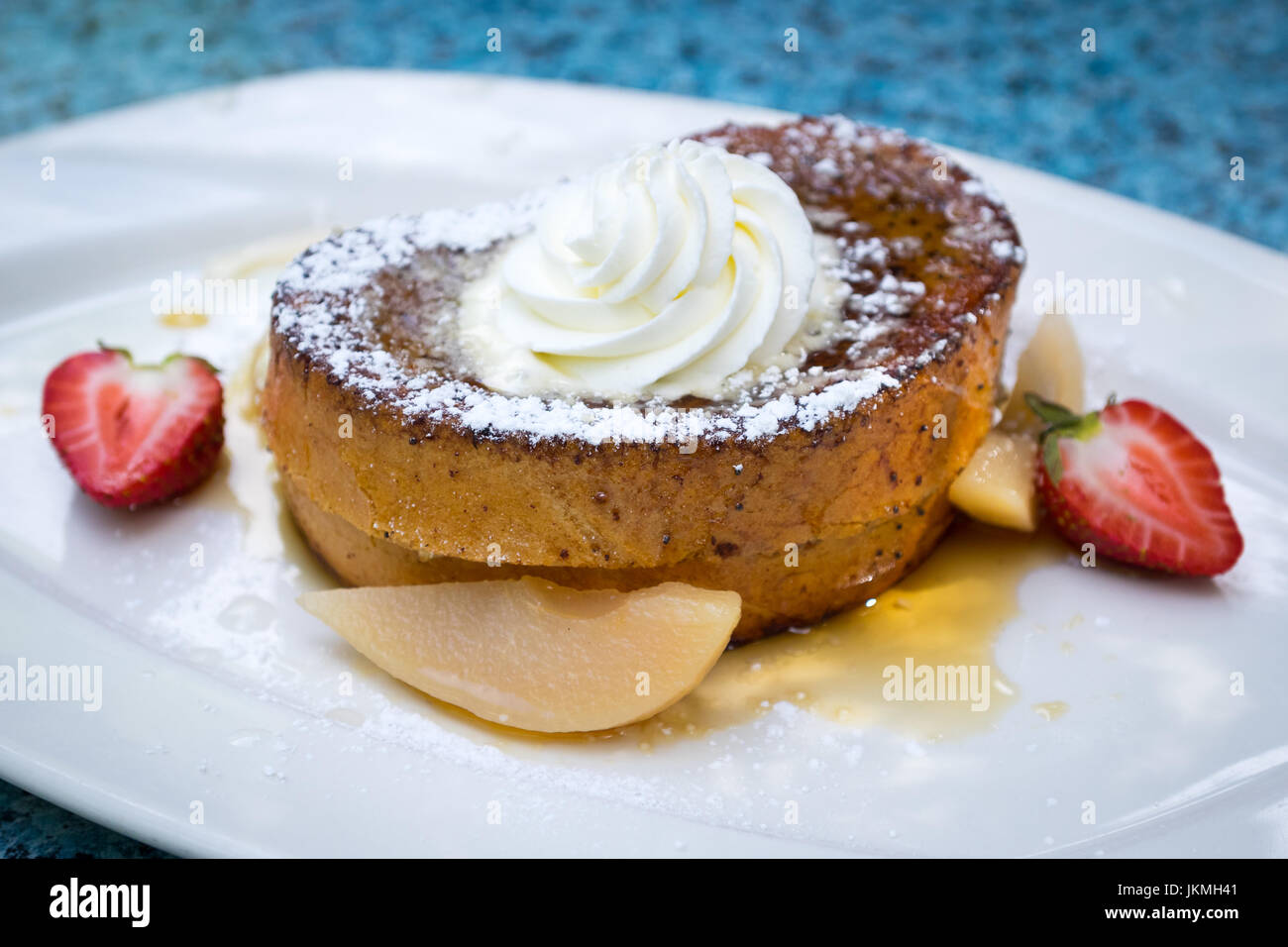 Beautifully plated cinnamon French toast (eggy bread) with whipped cream, maple syrup, vanilla poached pears, and strawberries. Stock Photo