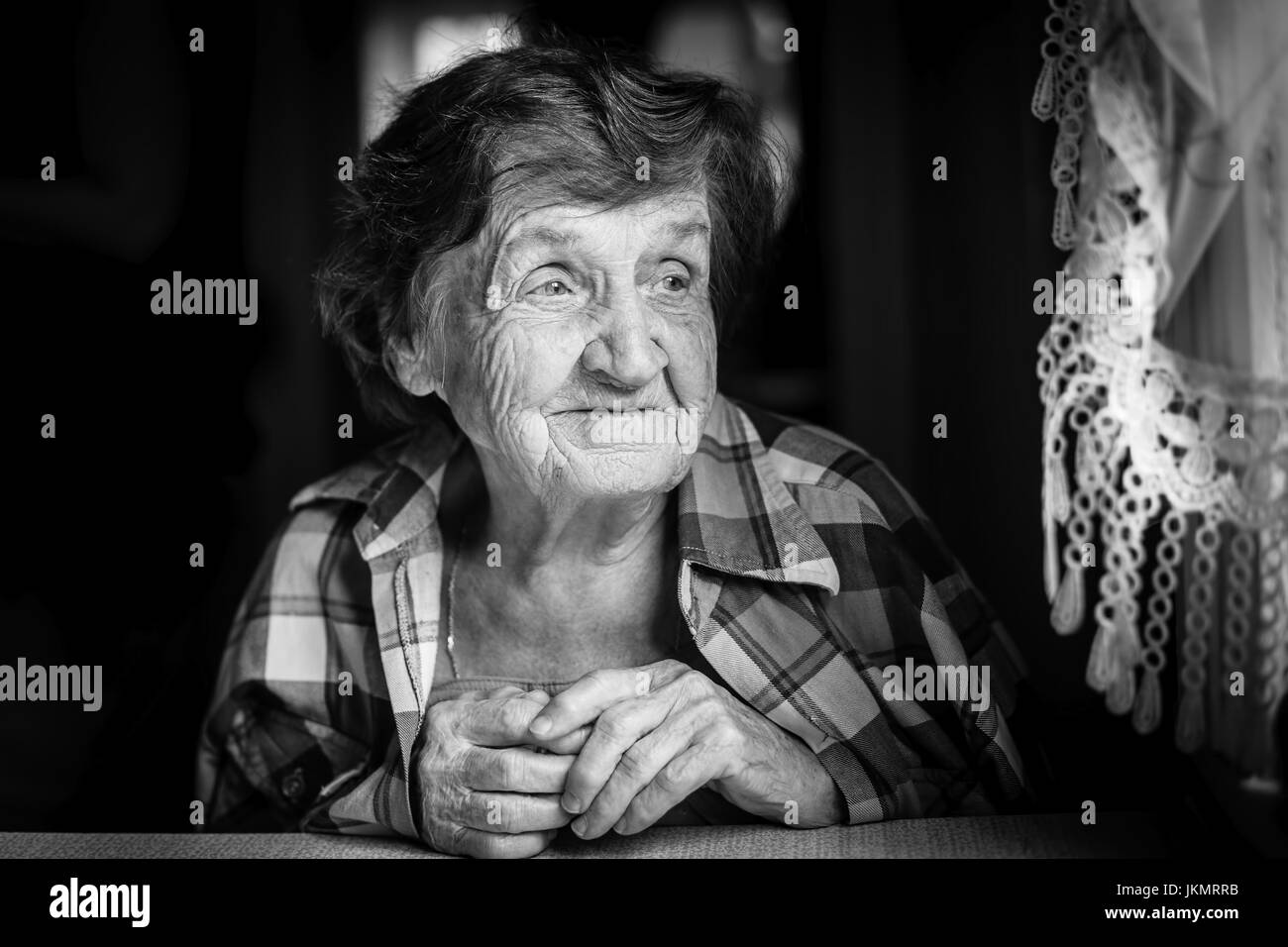 Portrait close-up of an elderly woman, in house by the window, a black-and-white photography. Stock Photo