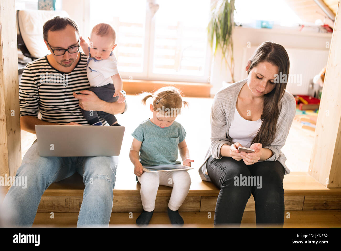 Young parents with little children and gadgets at home Stock Photo - Alamy
