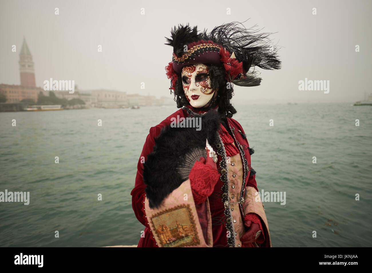 Female Mask wearer at the Carnival of Venice with red Coat and Red dress Stock Photo