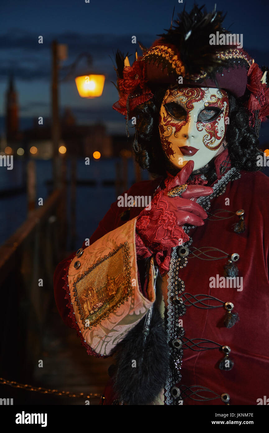 Female Mask wearer at the Carnival of Venice with red Coat and Red dress Stock Photo