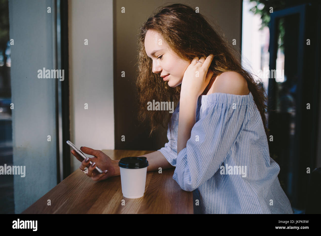 Young beautiful young girl drinking latte coffee in cafe against the window Stock Photo