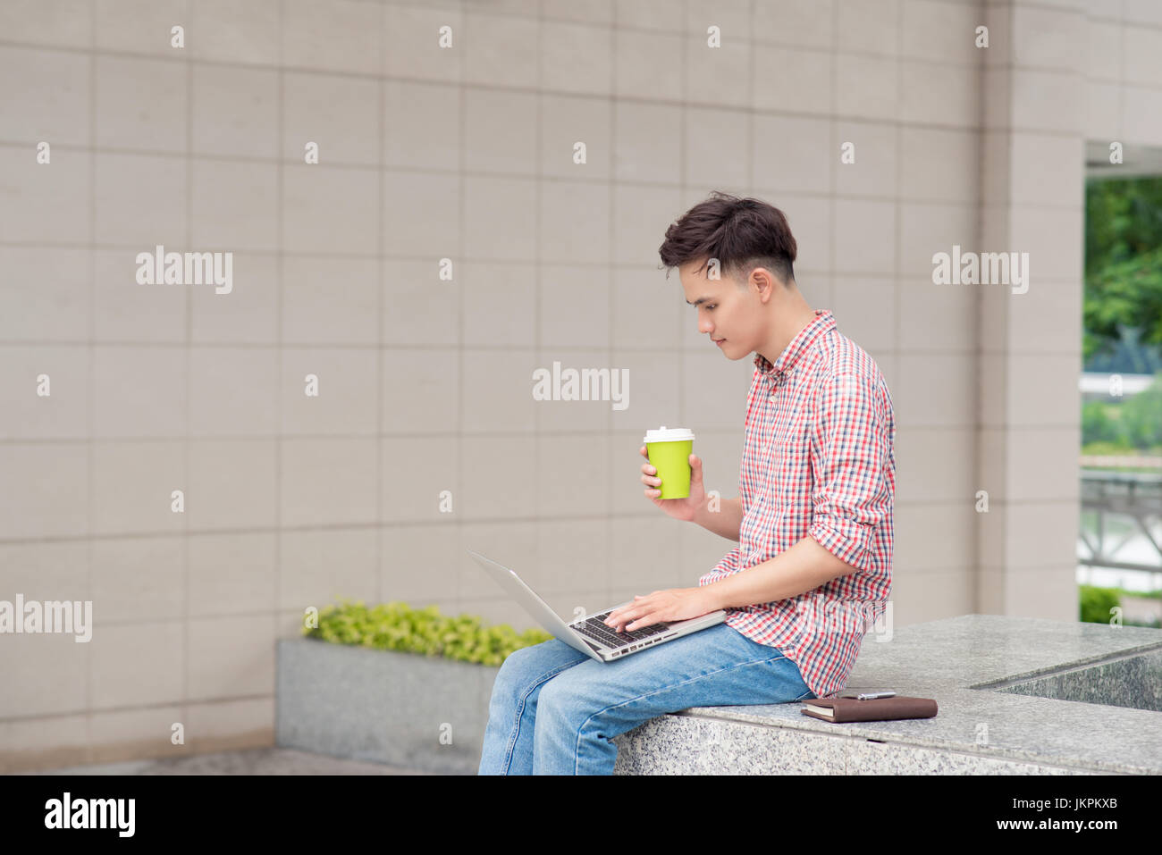 Portrait of a happy young man sitting on the city stairs with laptop ...