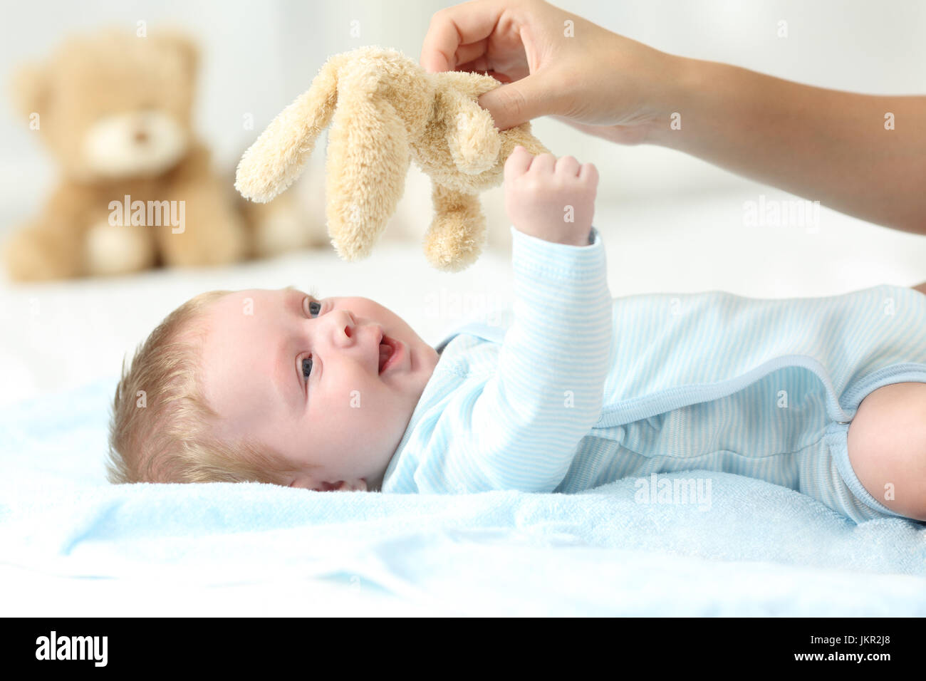 Mother hand holding a teddy and playing with her baby son on a bed Stock Photo