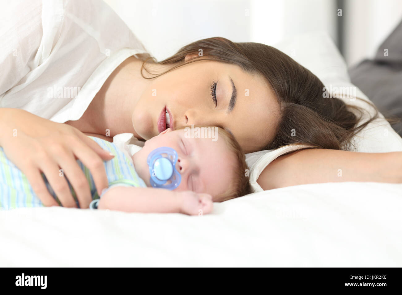 Tired mother sleeping with her baby on a bed at home Stock Photo