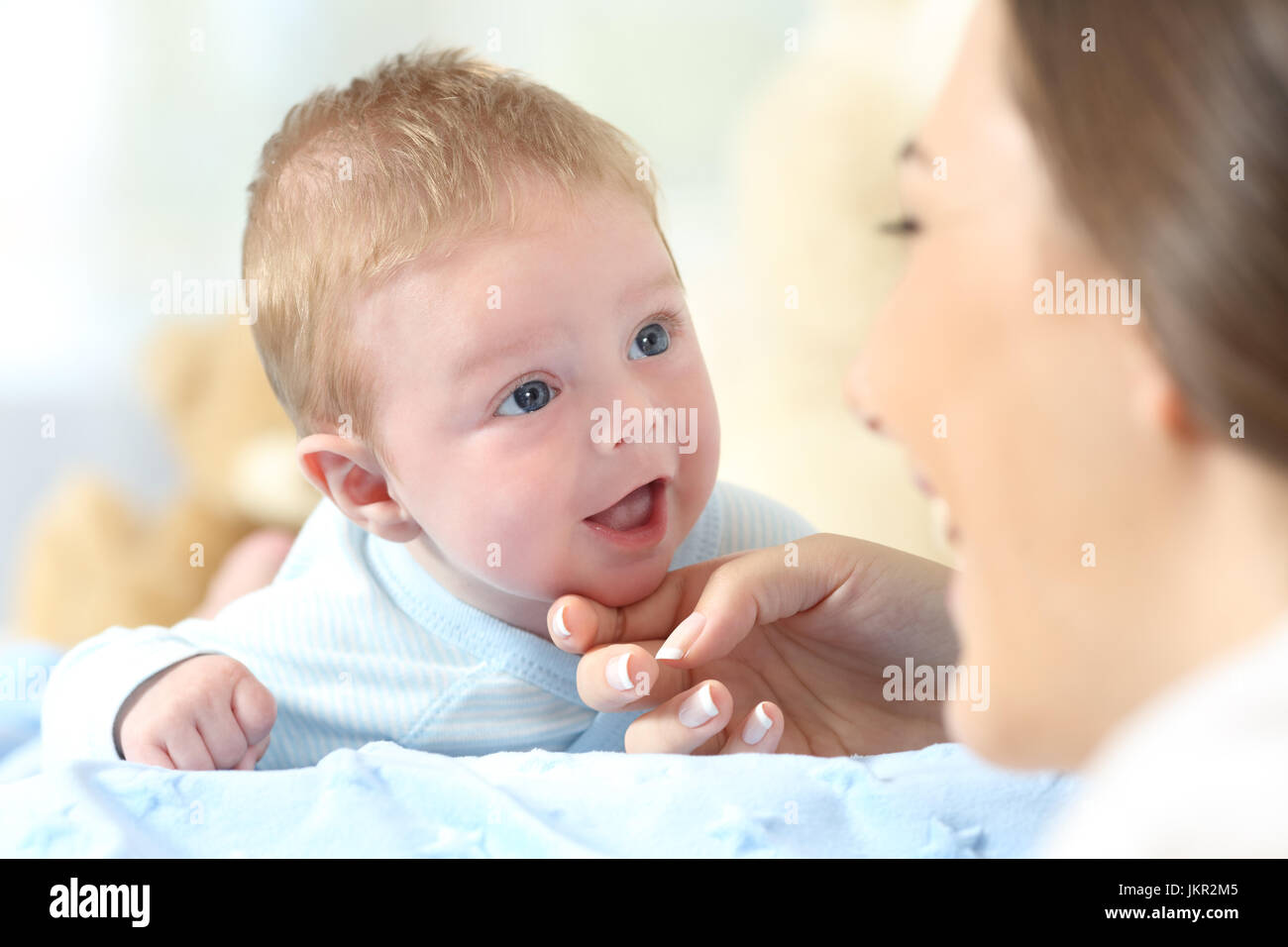 Close up portrait of a happy baby and mother looking each other on a bed Stock Photo