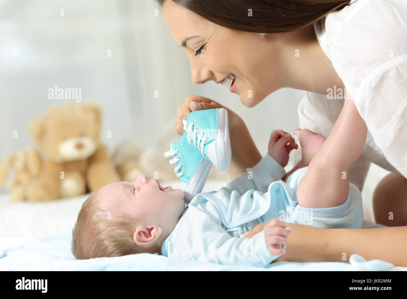 Happy mother showing a new shoes to her baby on a bed at home Stock Photo