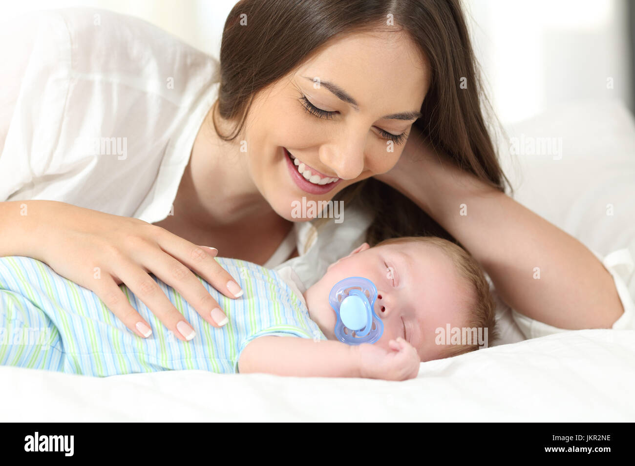 Proud mother watching her baby sleeping on a bed at home Stock Photo