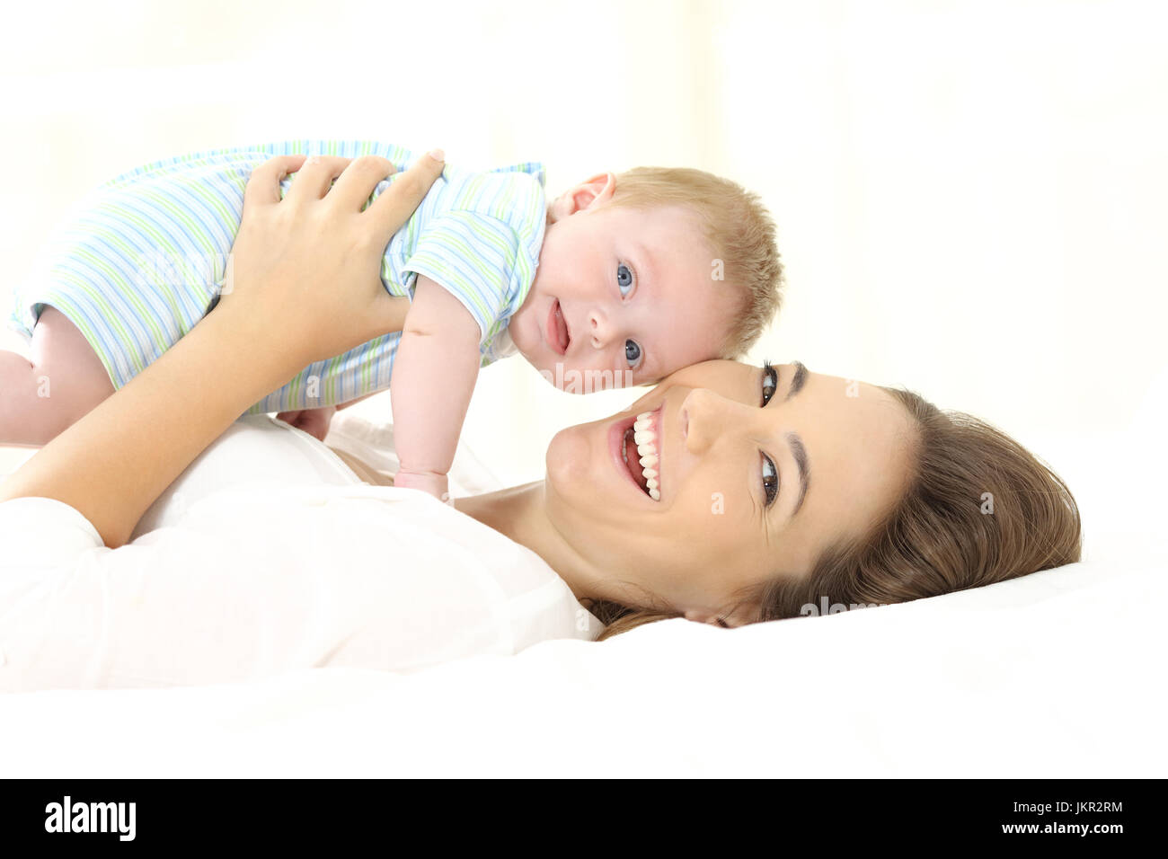 Happy mother and her baby looking at camera on a white bed and background Stock Photo