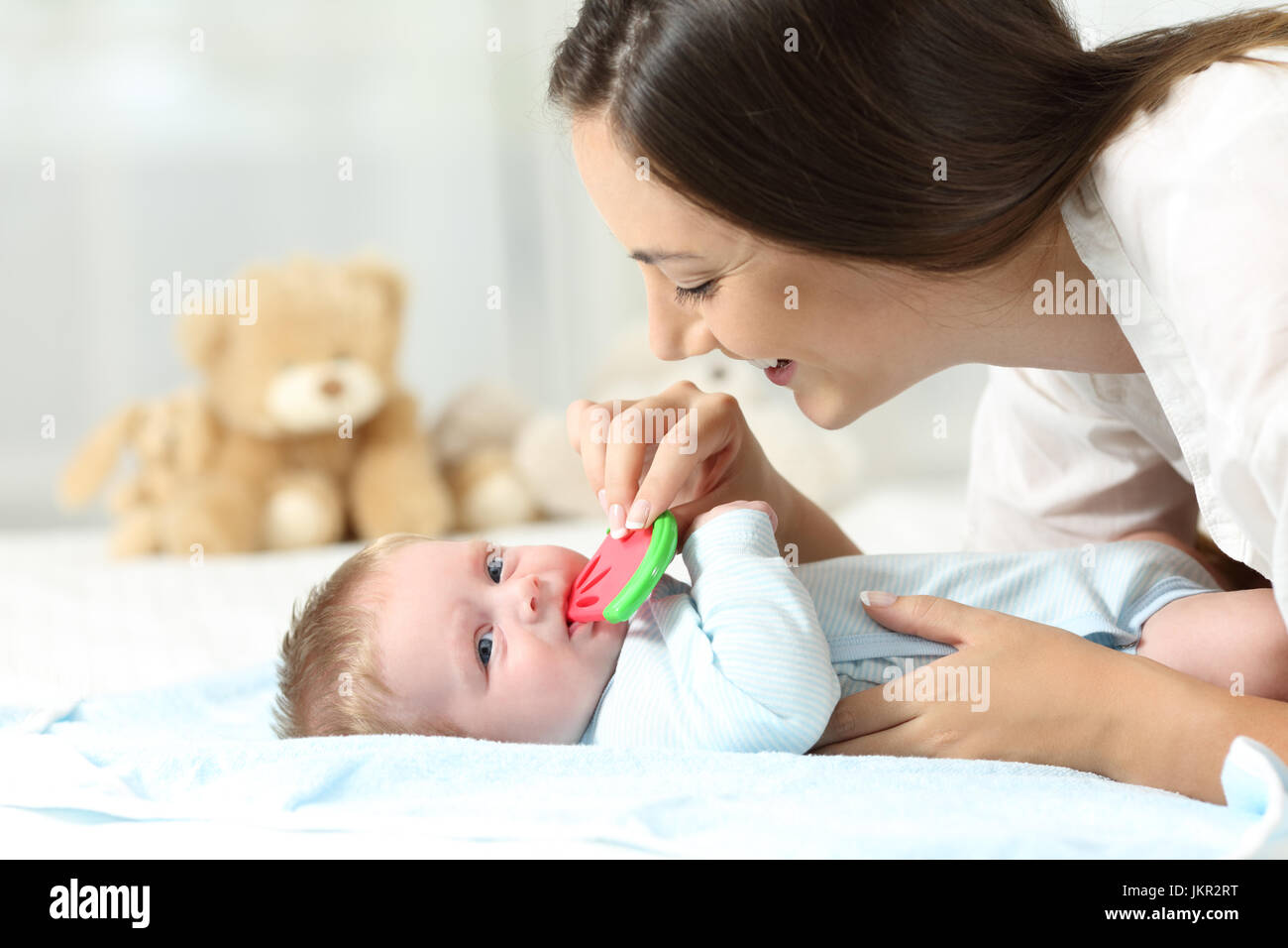 Happy mother giving a bitter to her baby on a bed Stock Photo