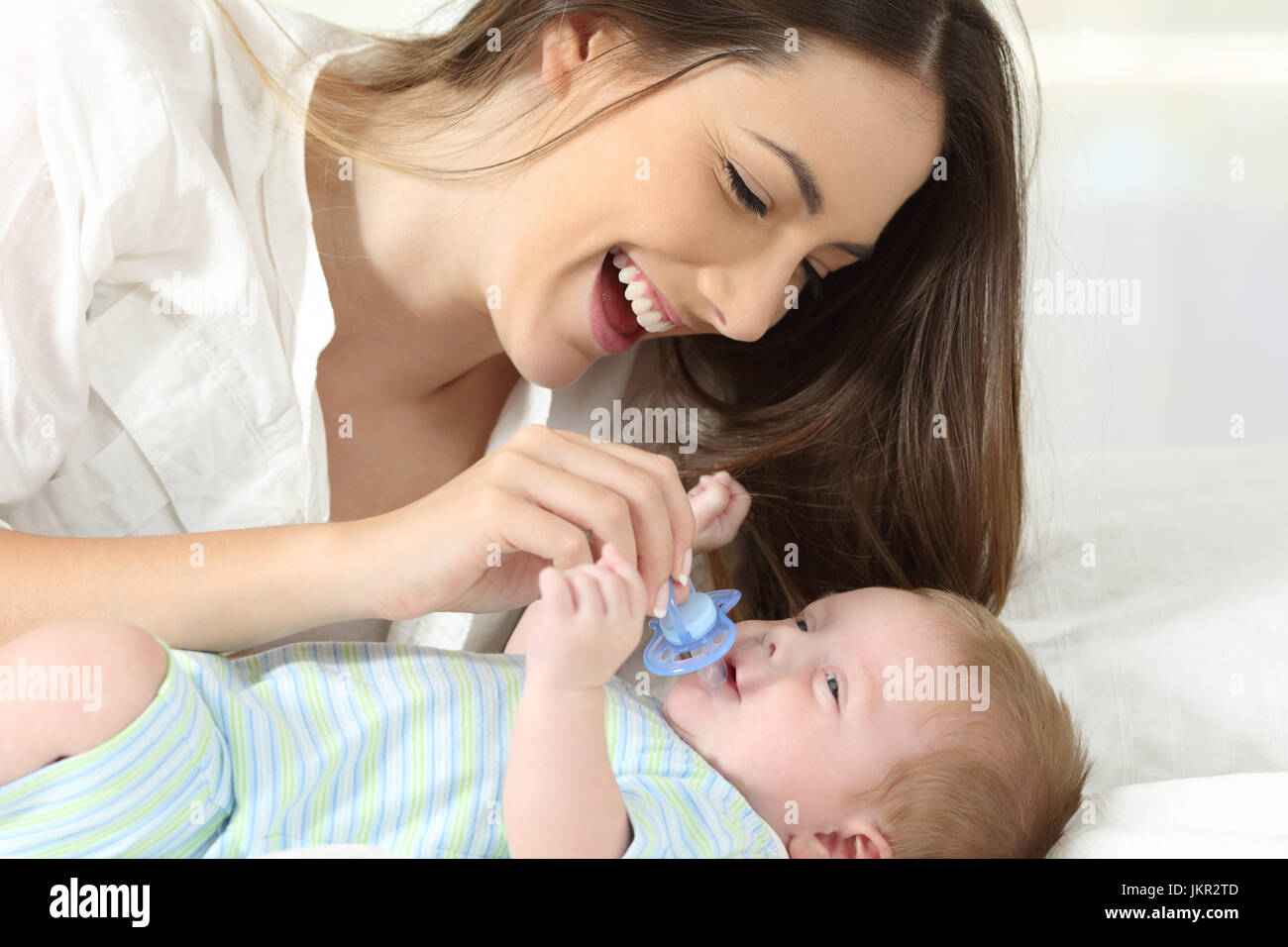 Happy mother giving a pacifier to her baby on a bed Stock Photo