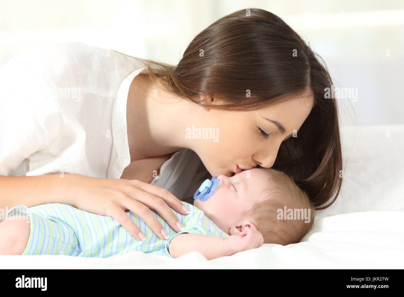 Side view portrait of an affectionate mother kissing her baby sleeping on a bed Stock Photo