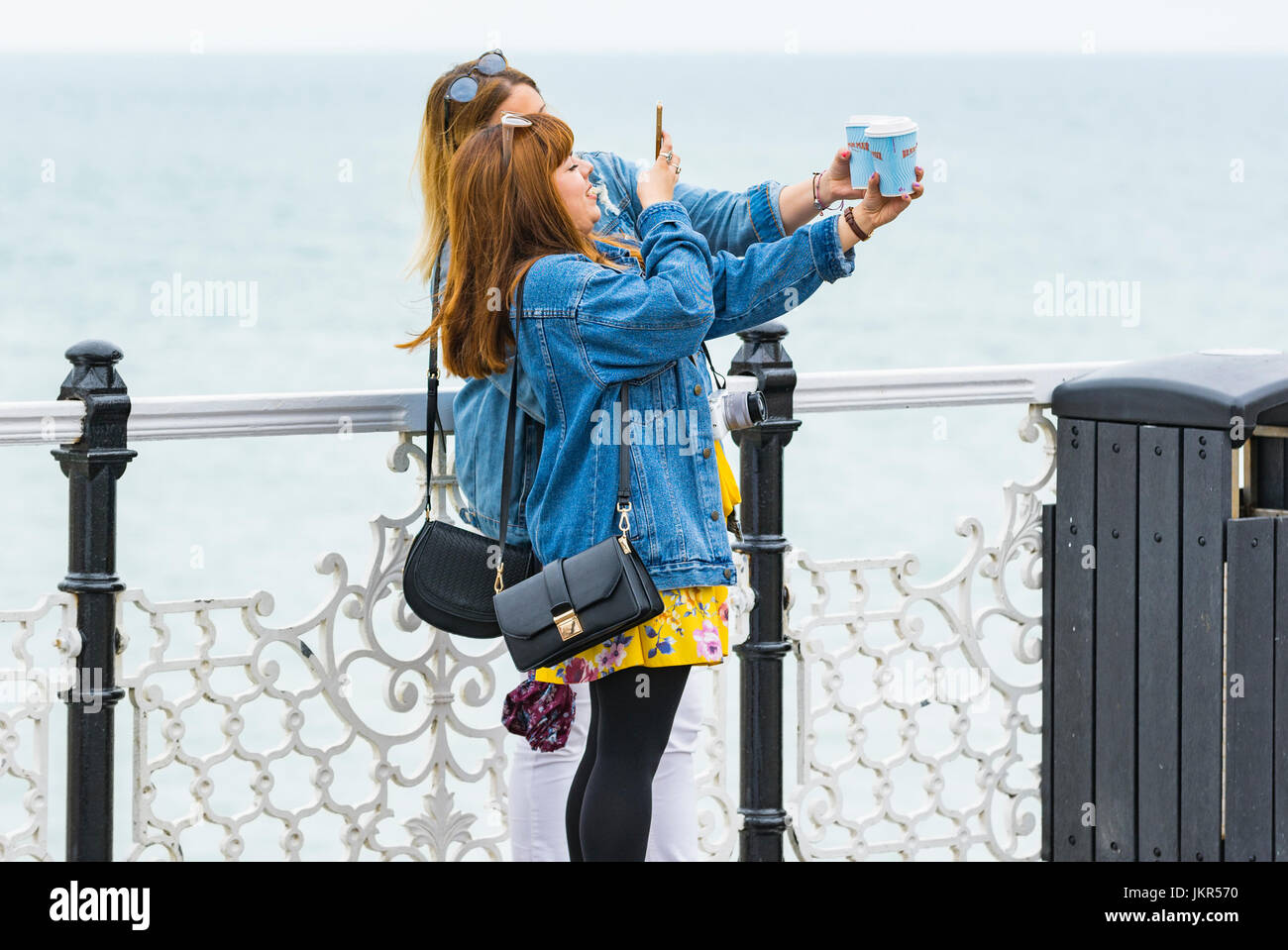 Young female friends enjoying a day out together taking photos at the seaside. Stock Photo