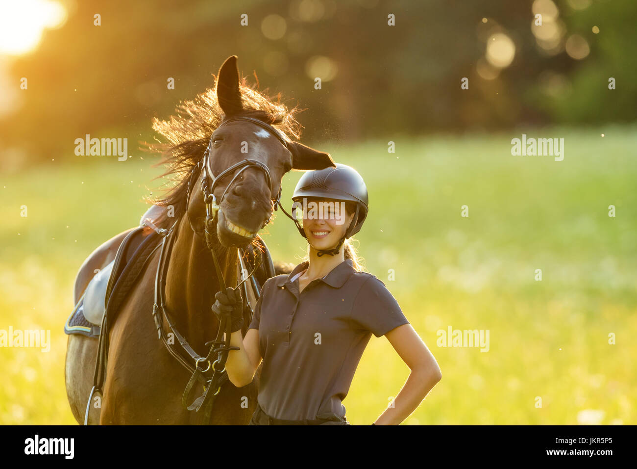 Young woman rider with her horse enjoying good mood in evening sunset light. Outdoor lifestyle photography Stock Photo