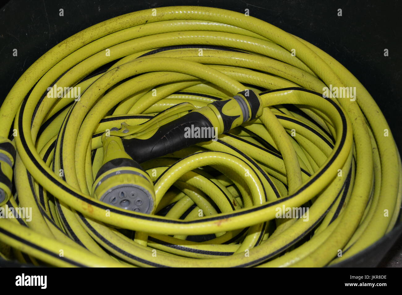 Close up of long length coiled hose hosepipe with multi spray hose gun watering nozzle attachment re watering the garden cleaning the car Stock Photo