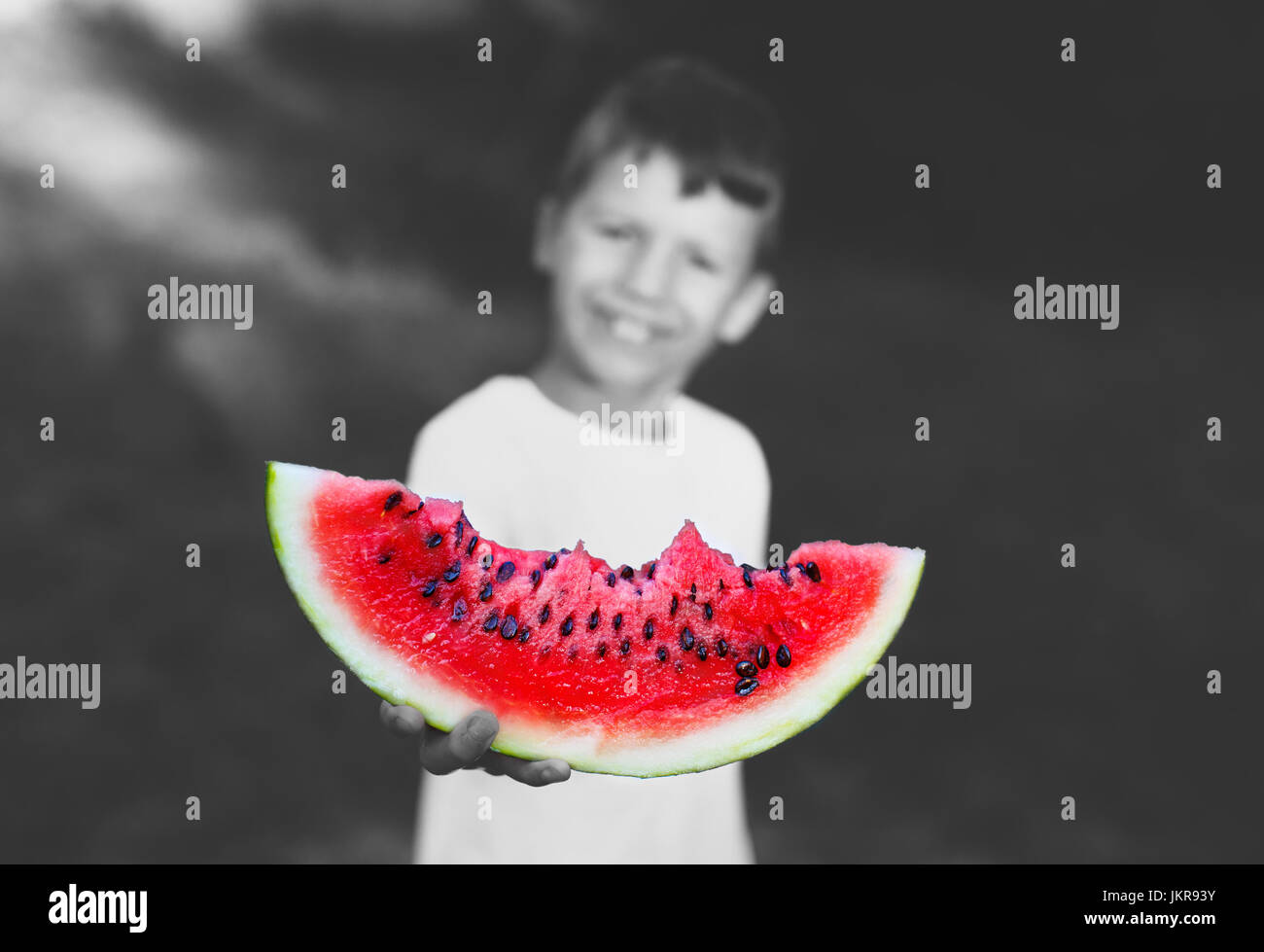 Little boy holding slice of watermelon outdoor, depth of field, selective colored black and white Stock Photo