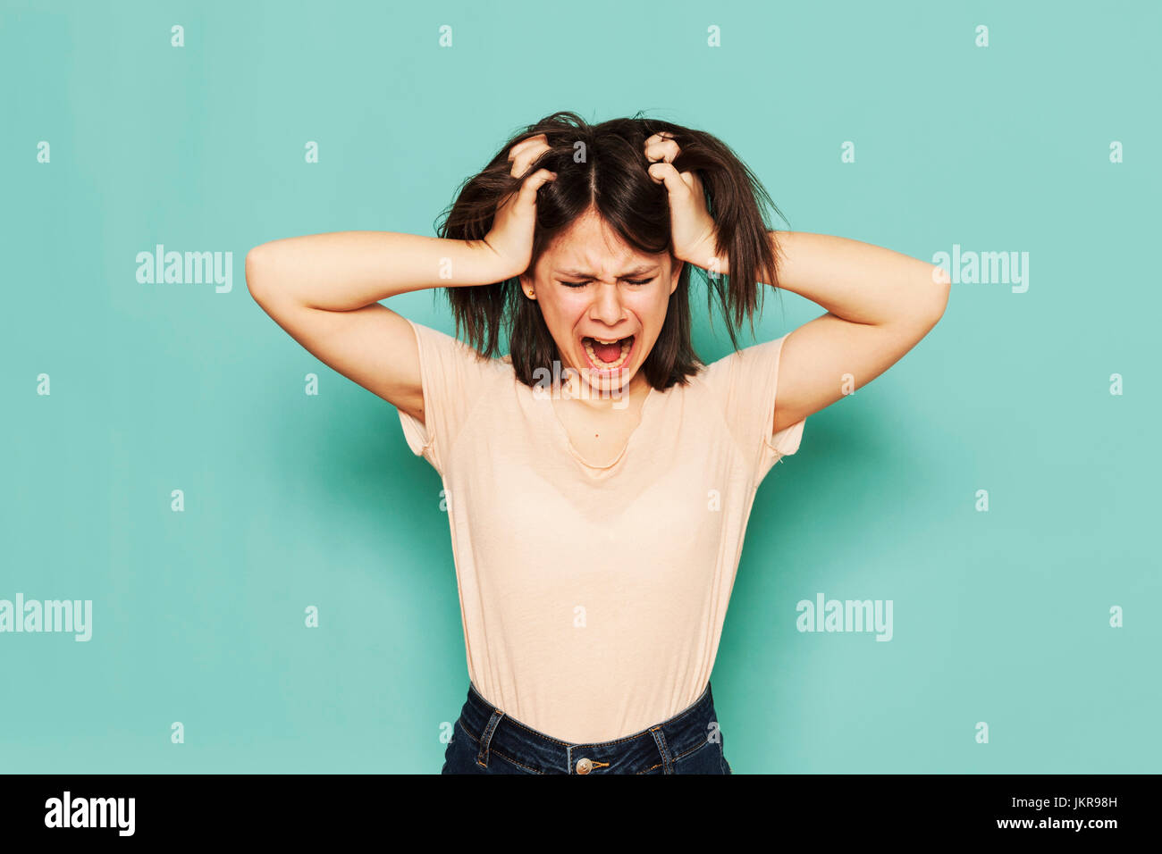Irritated girl shouting with hands in hair against turquoise background Stock Photo
