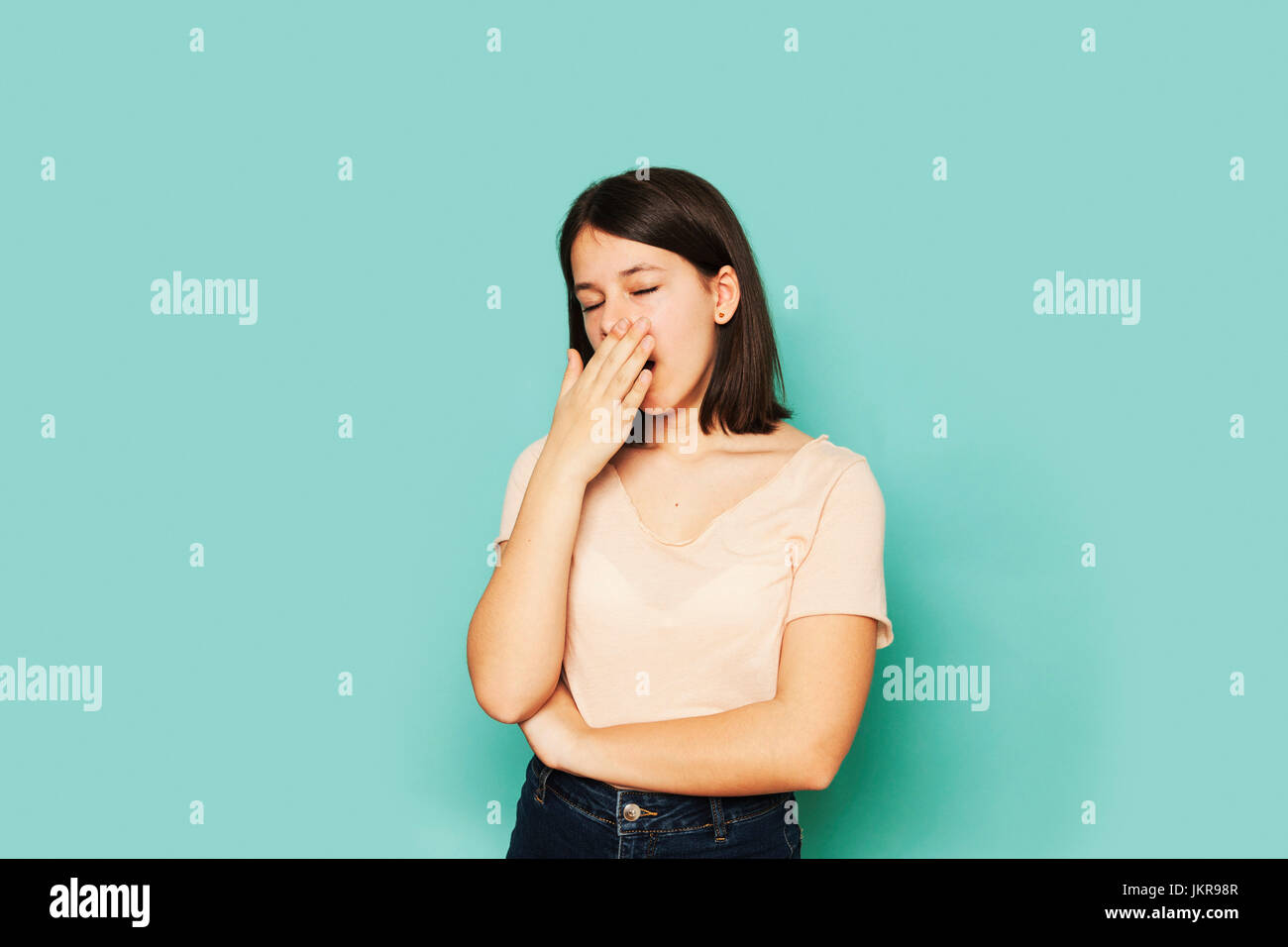 Tired girl yawning while standing on turquoise colored Stock Photo