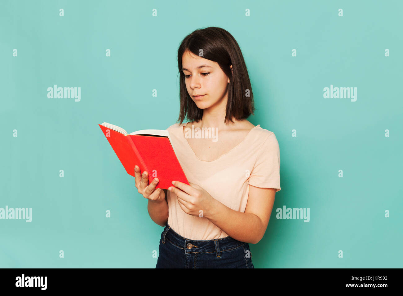Girl reading novel against turquoise background Stock Photo