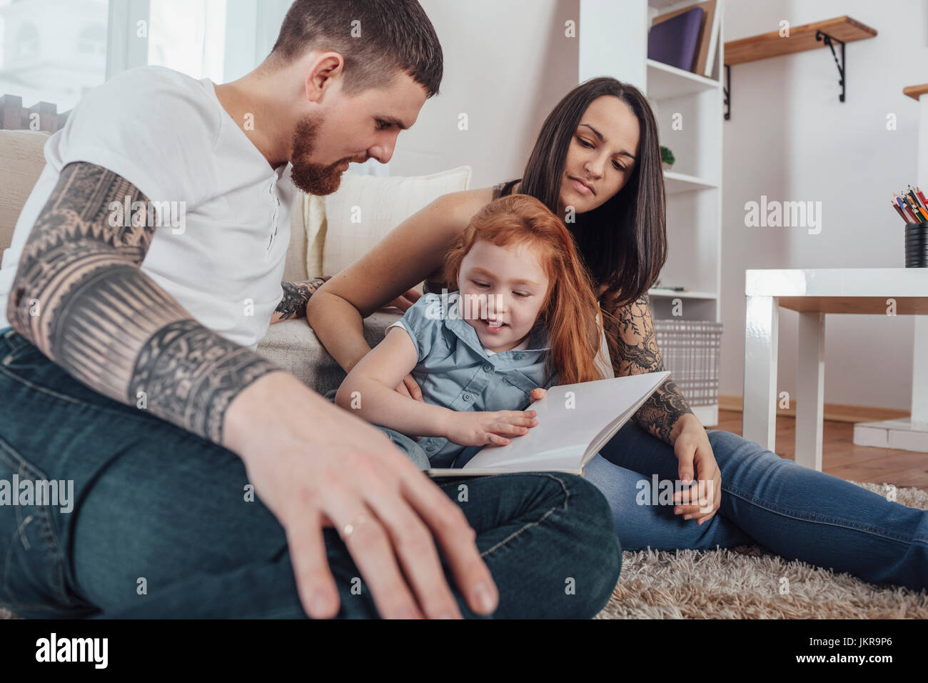 Parents looking at daughter reading book while sitting on carpet at home Stock Photo