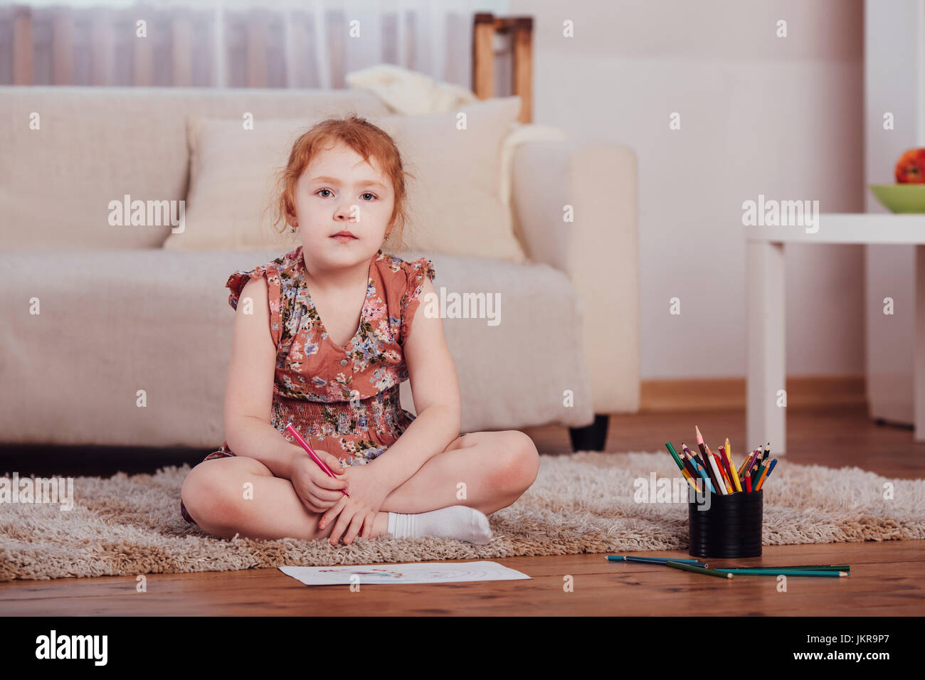 Portrait of smiling girl drawing while sitting on carpet in living room at home Stock Photo