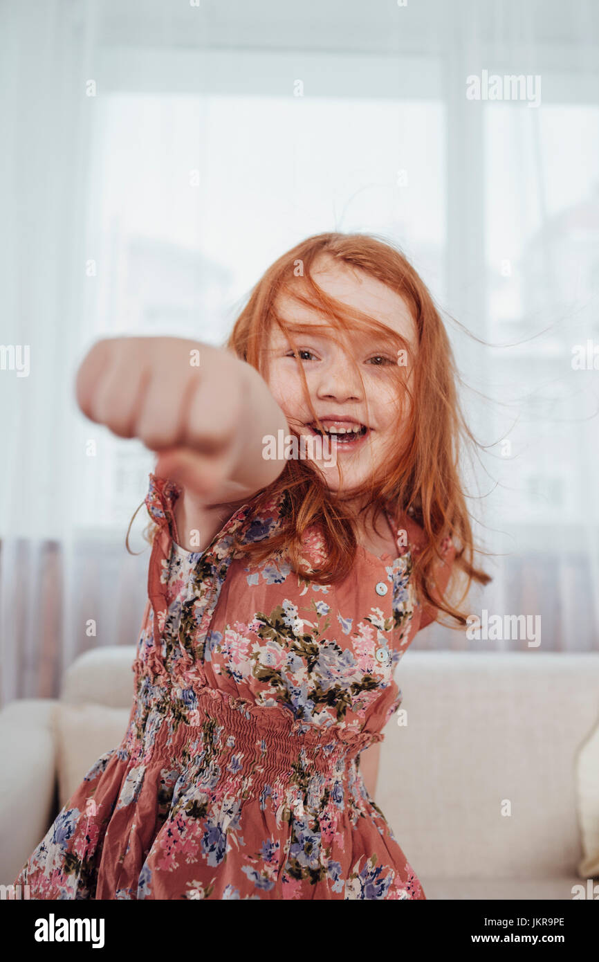 Portrait of cheerful girl punching while standing against sofa in living room Stock Photo