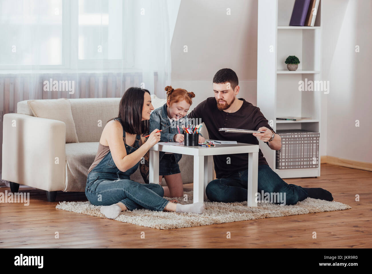 Happy parents drawing with daughter in living room at home Stock Photo