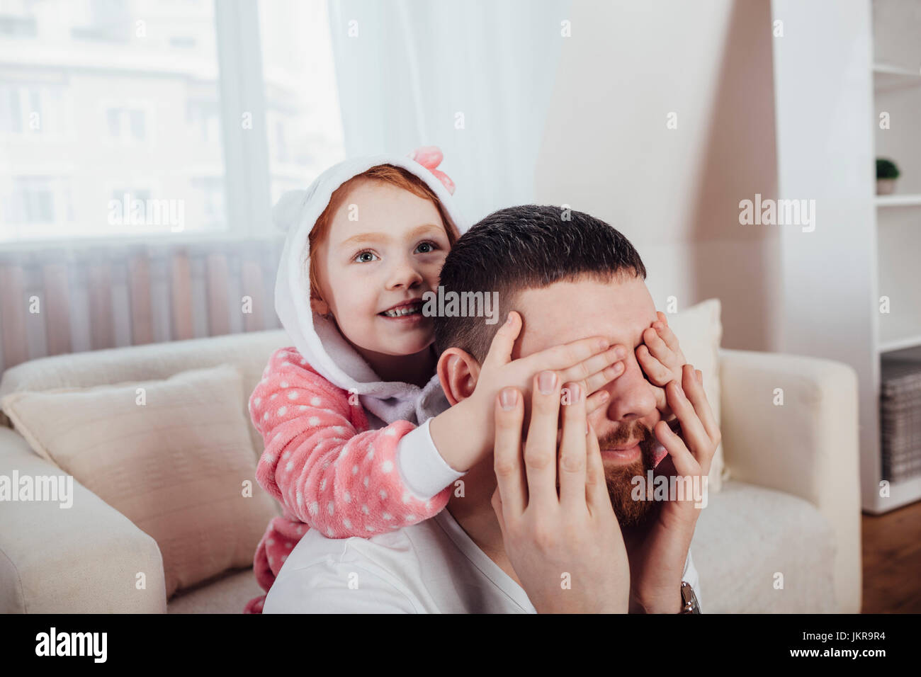 Daughter covering father's eyes while playing in living room at home Stock Photo