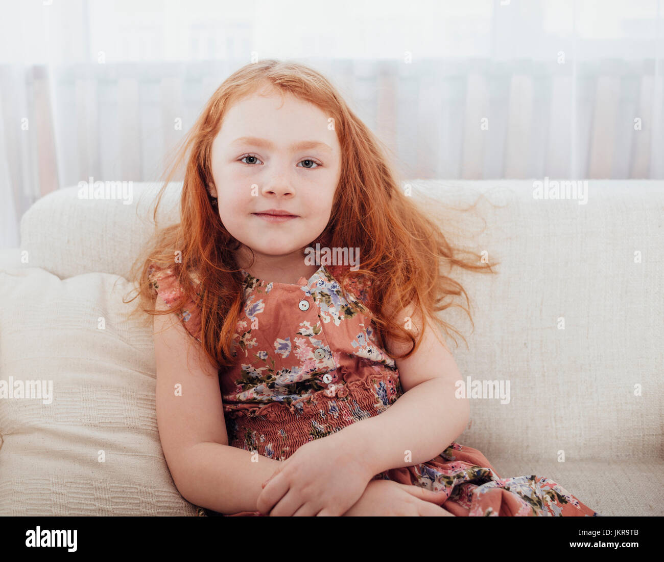 Portrait of smiling girl with redhead sitting on sofa at home Stock Photo