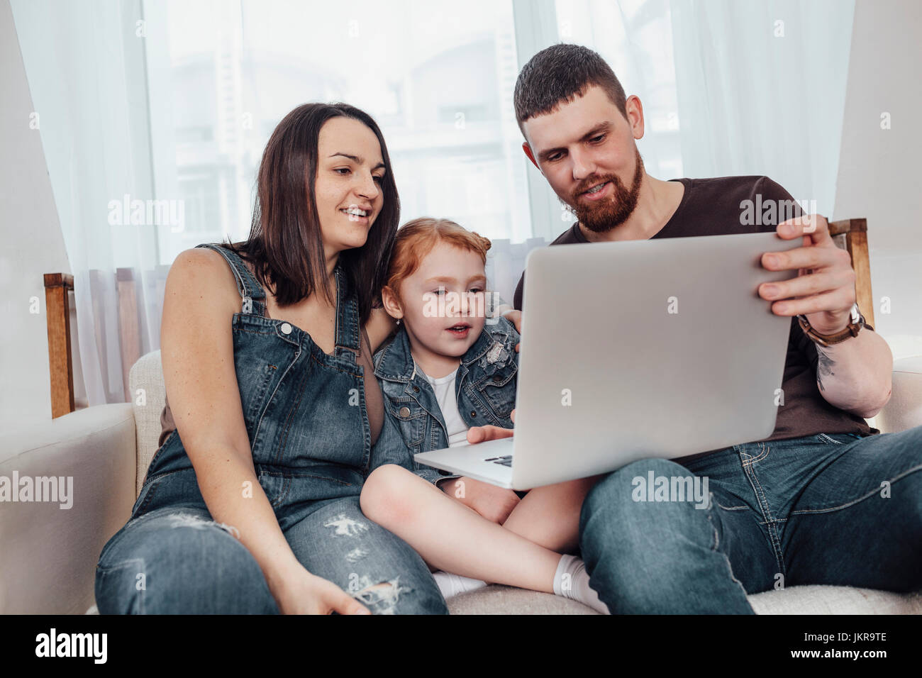 Father and mother with daughter looking at laptop while sitting on sofa Stock Photo