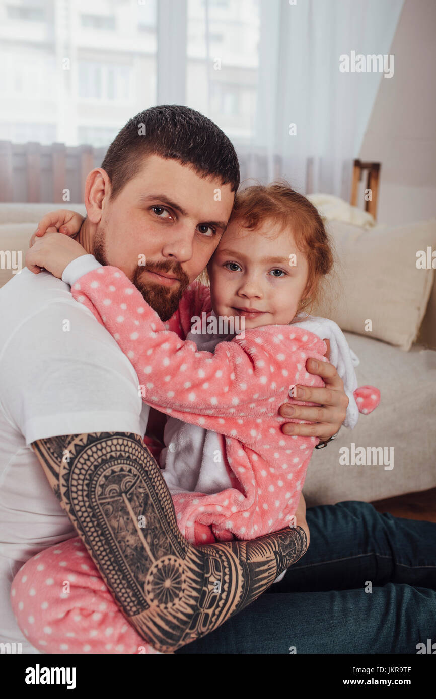 Portrait of smiling father and daughter embracing while sitting on sofa at home Stock Photo