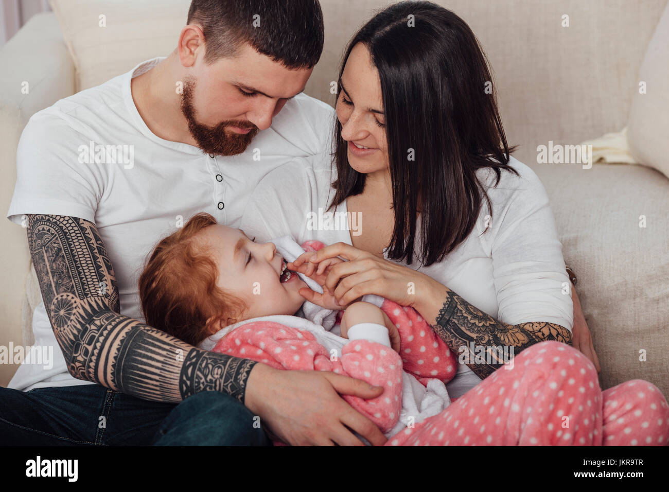Smiling parents playing with daughter while sitting on sofa at home Stock Photo