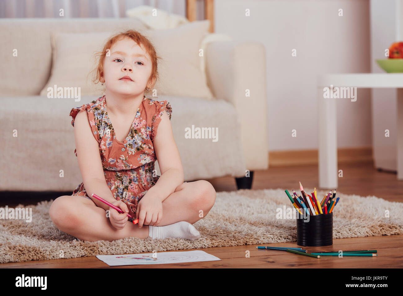 Thoughtful girl drawing while sitting on carpet in living room at home Stock Photo