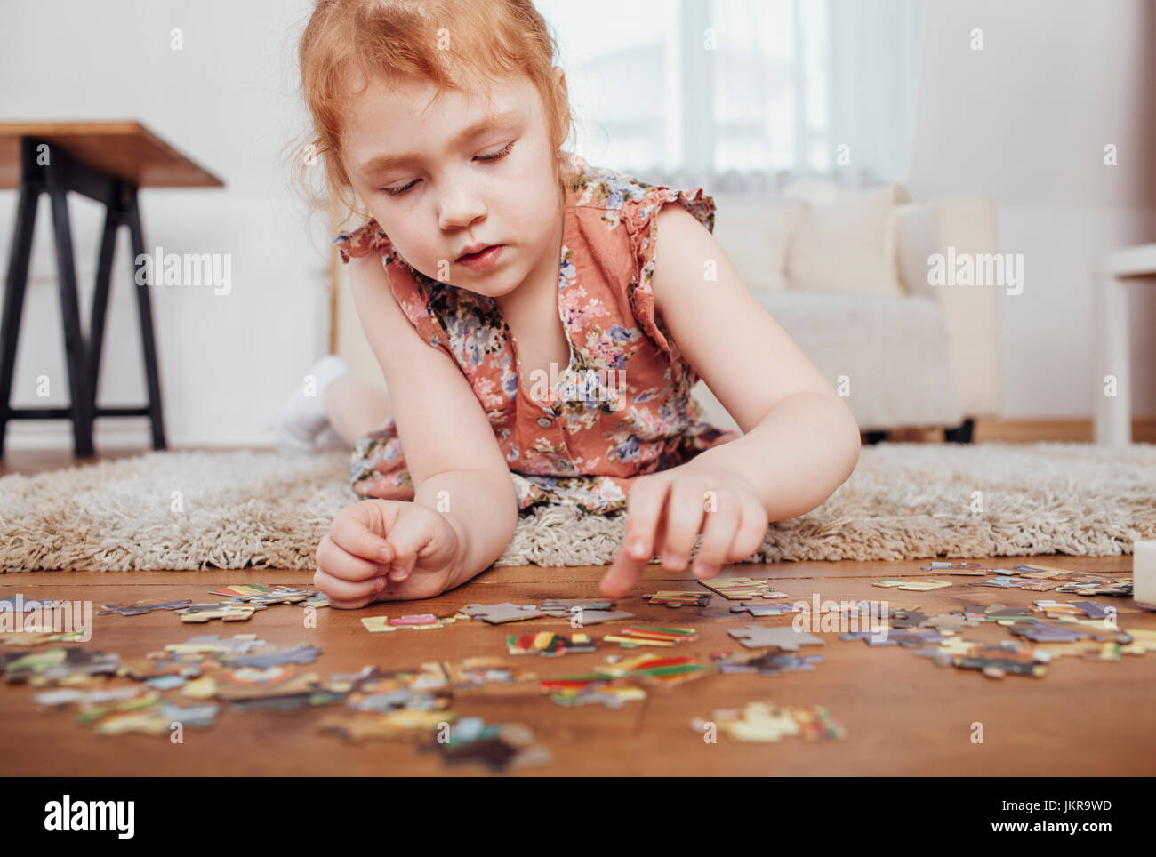 Girl playing with puzzle pieces while lying on carpet at home Stock Photo