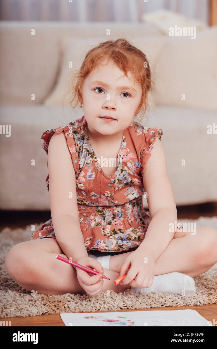 Cute girl drawing while sitting on carpet in living room at home Stock Photo