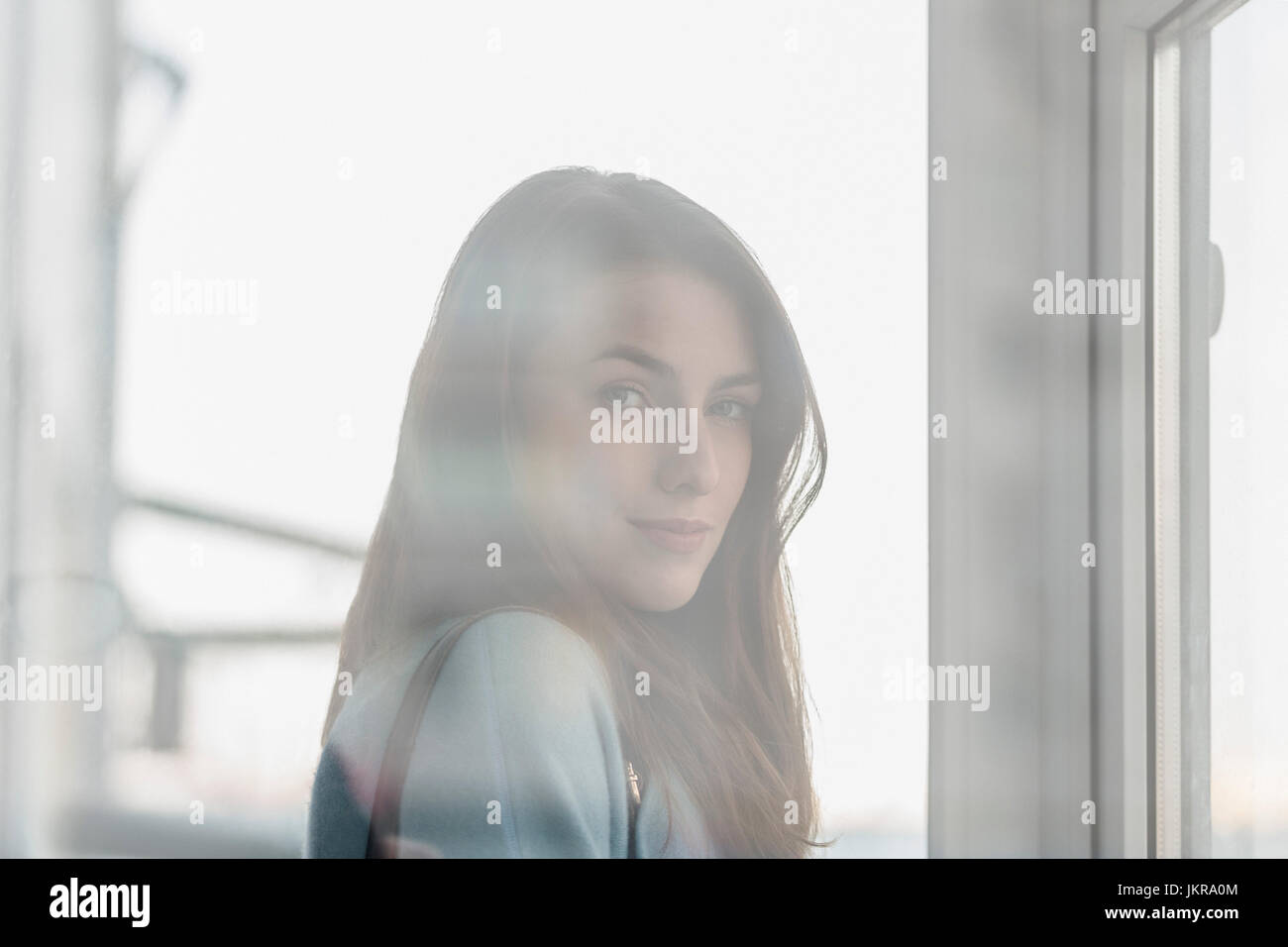 Portrait of young beautiful woman with long hair seen through glass window Stock Photo