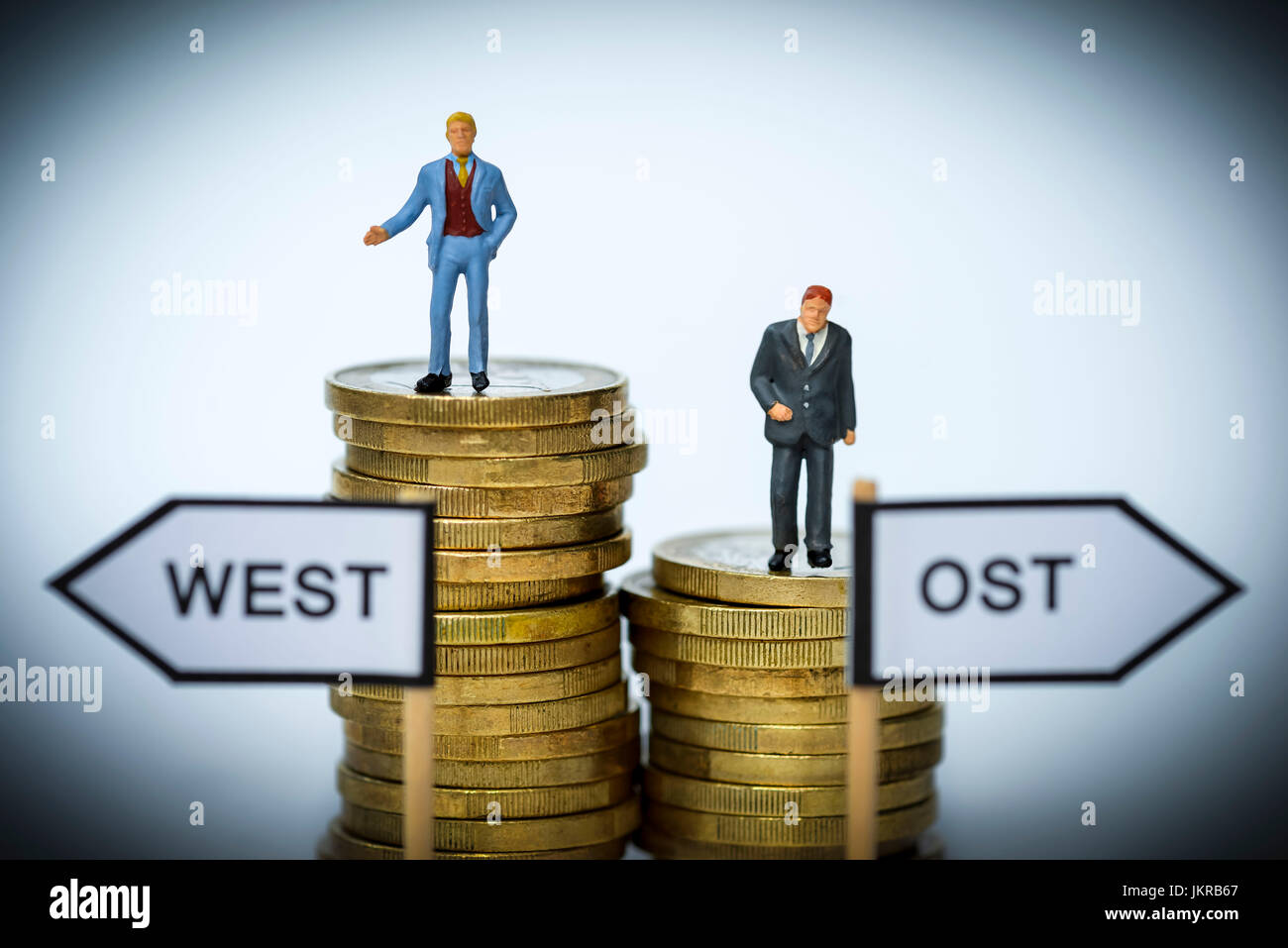 Businessmen-miniature figures on coin piles, unequal salaries in west country and Eastern Germany, Geschäftsmänner-Miniaturfiguren auf Münzstapeln, un Stock Photo
