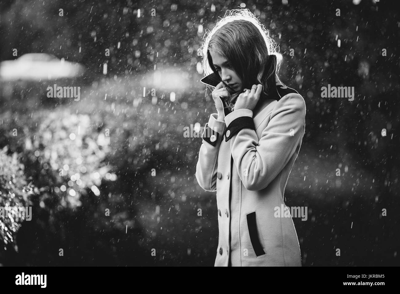 Thoughtful teenage girl wearing overcoat standing outdoors in rain Stock Photo