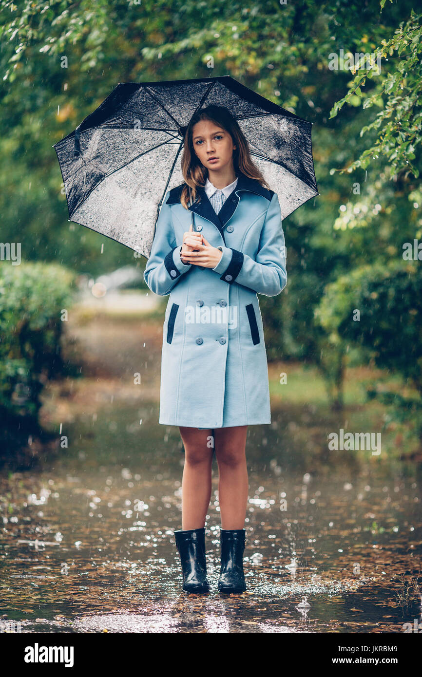 Portrait of teenage girl holding umbrella while standing on pathway amidst trees in rain Stock Photo