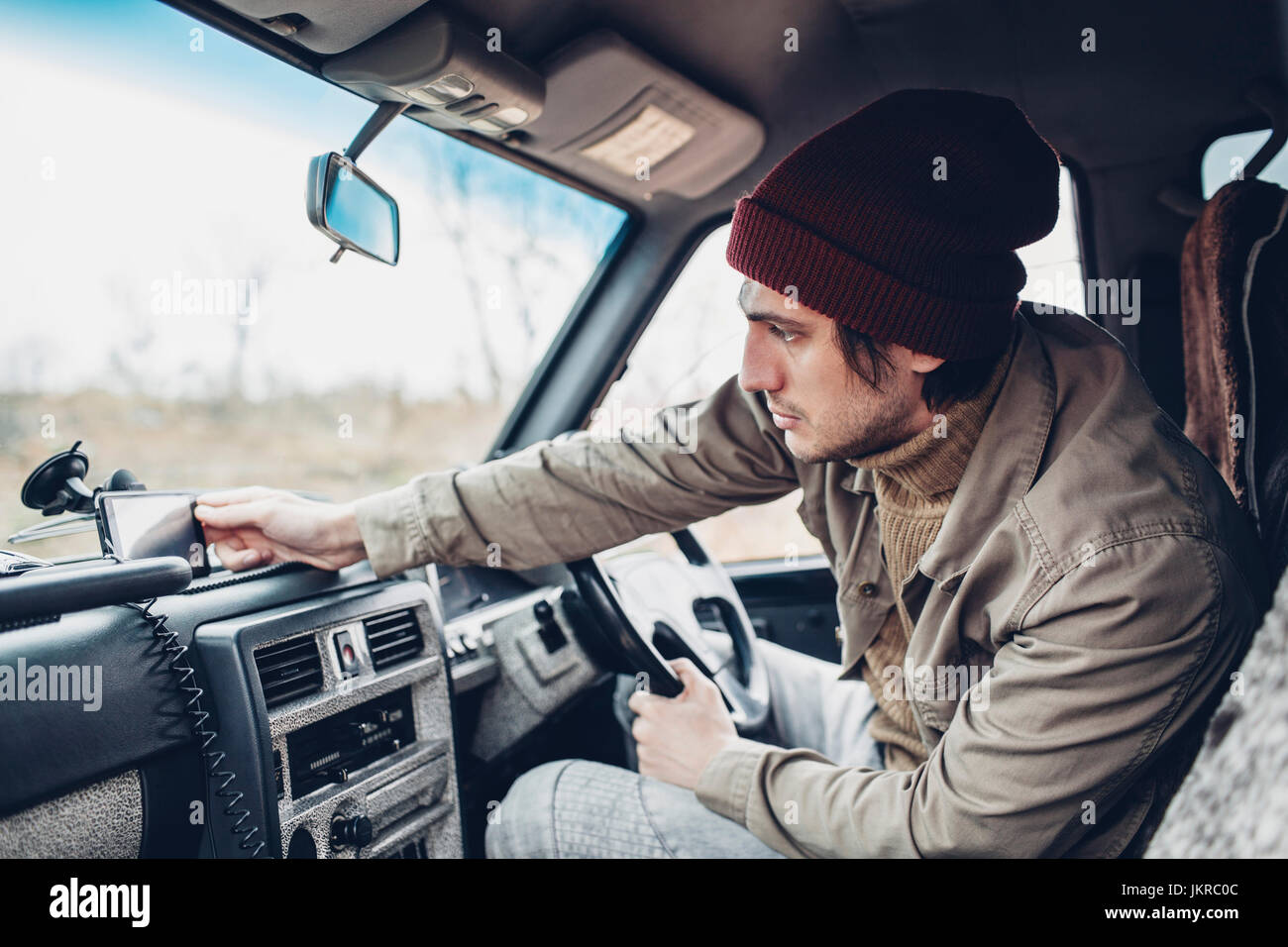 Man wearing knit hat and adjusting smart phone on dashboard of sports utility vehicle Stock Photo