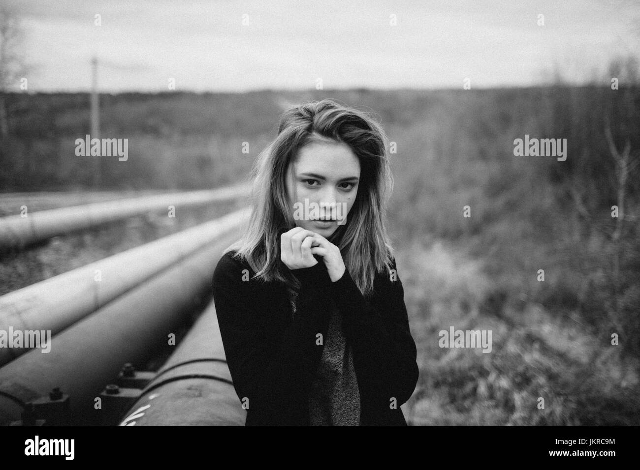 Portrait of teenage girl with hands clasped standing by pipes on field against sky Stock Photo