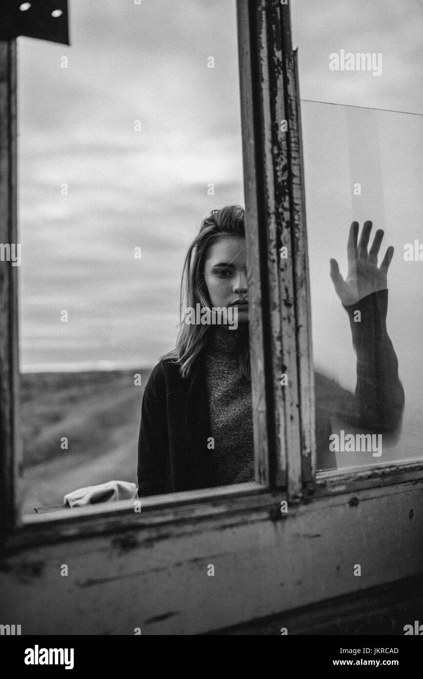 Thoughtful teenage girl standing by glass window of old lookout tower against sky Stock Photo